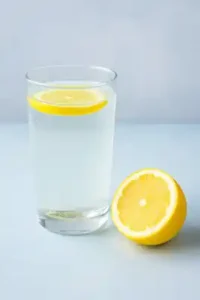Copo de vidro com água e rodelas de limão sobre superfície clara